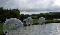 Three people inside water zorbs walk on water close to the edge.