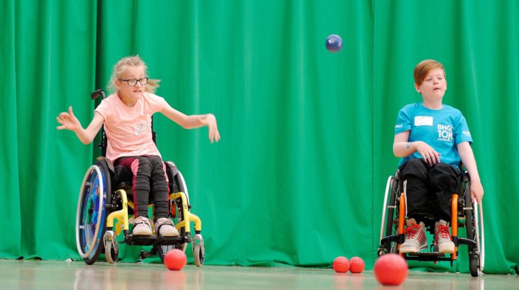 Two children playing boccia. One child is in action throwing the blue ball.