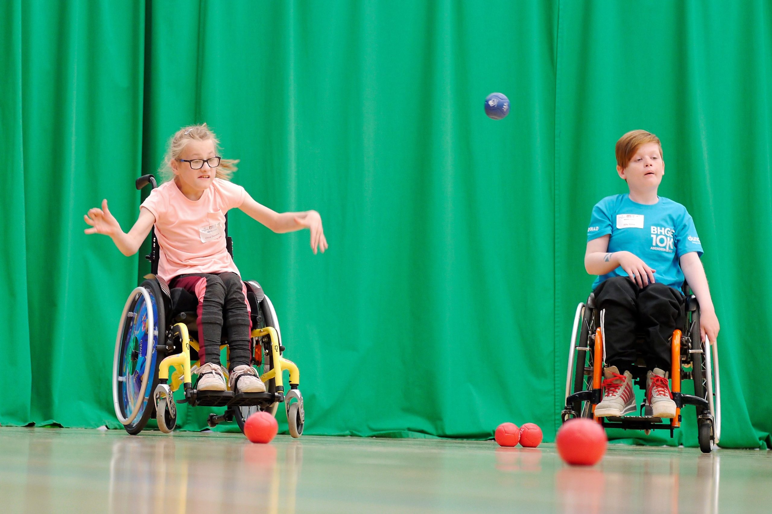 Two children playing boccia. One child is in action throwing the blue ball.