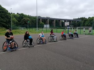 A group of young people playing wheelchair basketball line up along an outdoor court.